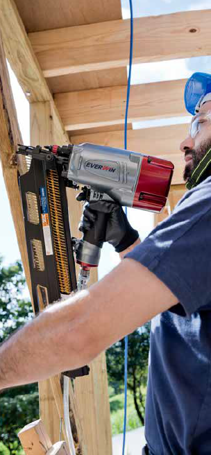 A construction worker using a heavy-duty framing nailer to secure wooden beams on an outdoor structure.