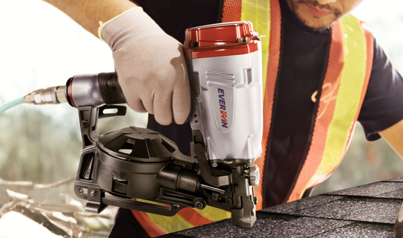 A construction worker using a roofing nailer to install and secure asphalt shingles on a rooftop.