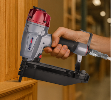 Close-up of a finish nail gun being used on indoor wood molding, demonstrating its precision for delicate woodworking finishes.